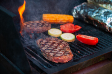 Beef steaks with vegetables on the grill with flames