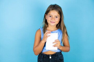 Young beautiful child girl over isolated blue background smiling and showing blank notebook in her hand