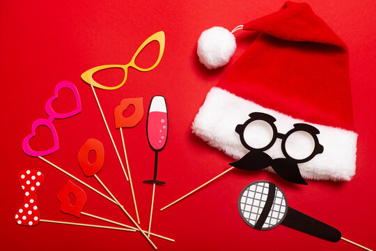 A red color banner with a Santa hat with a white pompom and a face from glasses and mustache. A props for fun photos at a New Year corporate festive or a karaoke party for girl team