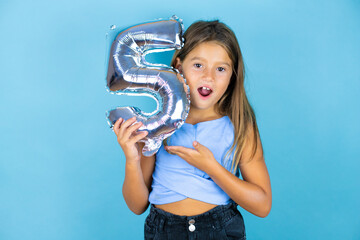Young beautiful child girl over isolated blue background surprised holding a number five. Celebration concept