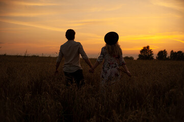 Fototapeta na wymiar Silhouettes of a man and a woman in a field against the sunset sky. A man and a woman hold hands. Love and relationships. 
