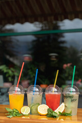 Summer refreshing non-alcoholic lemonades, row of plastic glasses to go on a bar counter