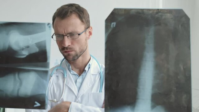 Close up of Caucasian male physician standing in the office at glass wall and examining x-ray images