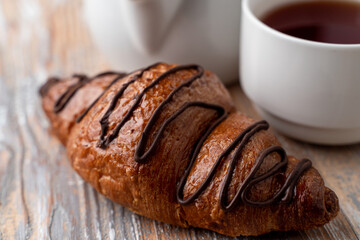 Puffy golden chocolate croissant on a wooden table with a cup of hot tea