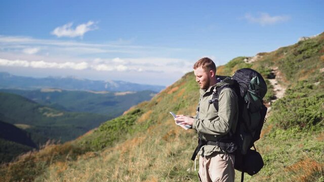 male tourist stands on the mountain, takes out a paper map, looking for a way