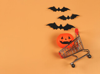 flat lay of  Halloween pumpkin on shopping cart  with black paper bats on orange background with...