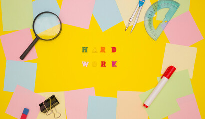 The concept of motivation, work. The words HARD WORK in the center on a yellow background, colored letters. Frame of empty note papers and stationery. Top view.