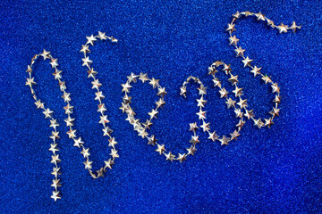 inscription "NEW" from silver garlands consisting of  stars on a blue background with small multi-colored sparkles