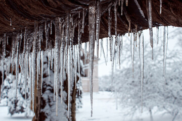Beautiful sharp icicles hang from the eaves of the roof. Ice with icicle, snowy winter landscape, background