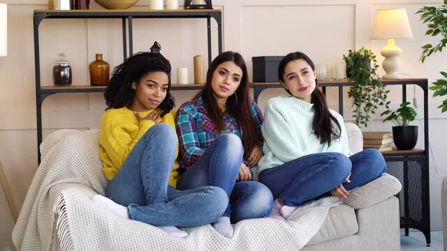 Young multiracial women in casual wear sitting together on sofa and watching sad motion picture on TV. Friends having movie night. Concept of entertainment