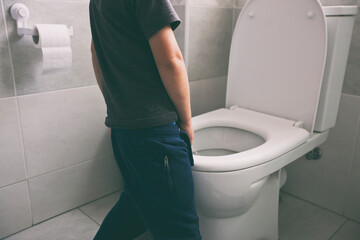 The boy is peeing into the toilet bowl in the restroom - obrazy, fototapety, plakaty