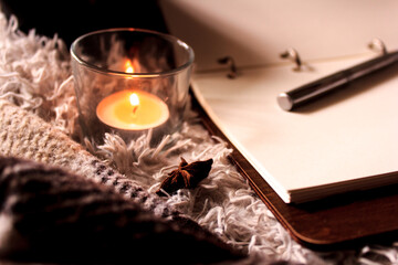 Hygge style. Warm blanket, burning candles, book for notes. vintage style, still life.
