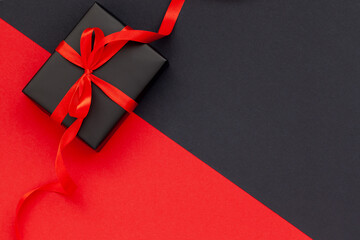 Black Friday concept. Top view of black gift box with red ribbon on black and red background with...