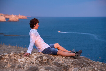 A young man stands on a rocky beach at sunset.