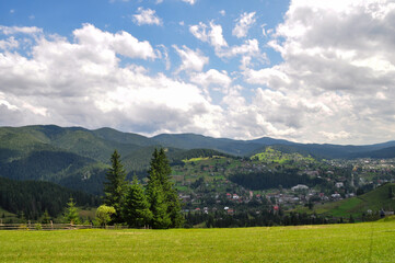 Fototapeta premium beautiful mountain landscape with bright clouds and sunlight in the sky, fluffy green spruces and indescribable beauty of the glade with residential buildings on the mountain slopes.