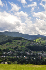 beautiful mountain landscape with bright clouds and sunlight in the sky, fluffy green spruces and indescribable beauty of the glade with residential buildings on the mountain slopes.