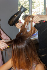Fototapeta premium two hairdresser girls with a hairdryer and a comb straighten hair, do hair styling. a girl came to a beauty salon to do her hair.