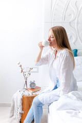 Young woman drinking coffee at home. Girl enjoying morning tea and relaxation. Beautiful interior in cozy bedroom.