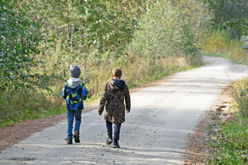 Two boys are walking along an autumn forest road