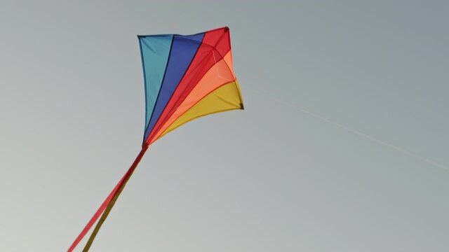 Flying kite against blue sky at sunset on sunny day in summer. Colored kite with an hangs in air. City kite festival. Tail of kite sways in wind. Childhood. Freedom. Toy. Relax