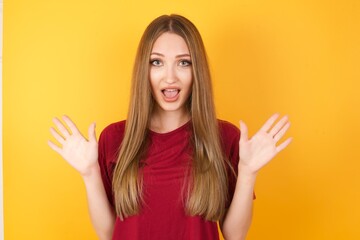 Optimistic Beautiful Young beautiful caucasian girl wearing red t-shirt over isolated yellow background raises palms from joy, happy to receive awesome present from someone, shouts loudly,