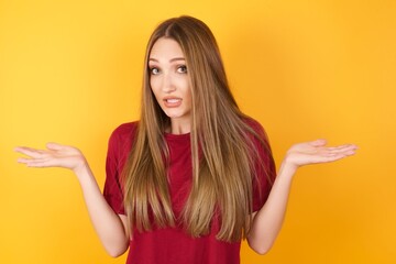 Clueless Beautiful Young beautiful caucasian girl wearing red t-shirt over isolated yellow background shrugs shoulders with hesitation, faces doubtful situation, spreads palms, Hard decision
