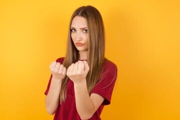 Beautiful Young beautiful caucasian girl wearing red t-shirt over isolated yellow background Ready to fight with fist defense gesture, angry and upset face, afraid of problem.