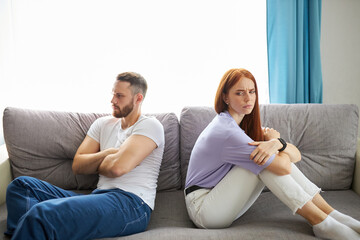 young caucasian couple lost in sad thoughts sitting together on sofa thinking feels troubled about...
