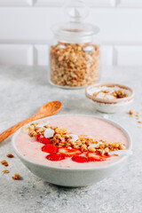 Healthy banana and strawberrie smoothie in a bowl with pieces of strawberries, granola and coconut chips