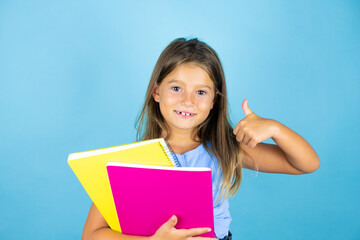 Obraz premium Young beautiful student child girl holding notebook over isolated blue background smiling and doing the ok signal with her thumb