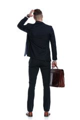 Rear view of confused businessman holding briefcase and scratching head