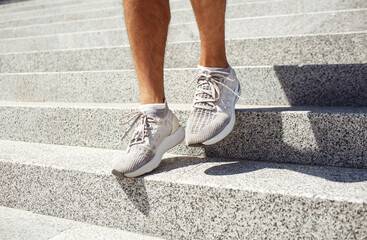 Fototapeta na wymiar Young man exercising outside. Picture of man's feet in sneakers walking down steps outside duing sunshine or daylight. Small training exercising on street. Shade from legs.