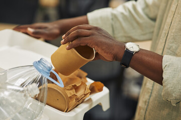 Close up of unrecognizable African-American man putting paper cup into waste sorting bin in office,...