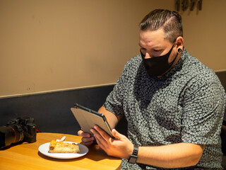 Shot of a man in a medical mask in a cafe  looking at his  tablet - new normal