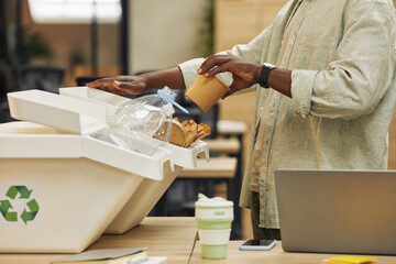 Cropped portrait of unrecognizable African-American man putting paper cup into waste sorting bin in...