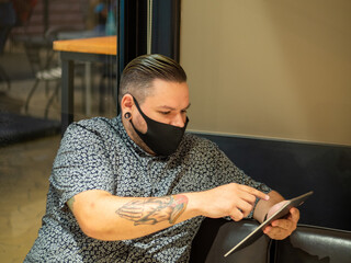 Shot of a man in a medical mask in a cafe  looking at his  tablet - new normal