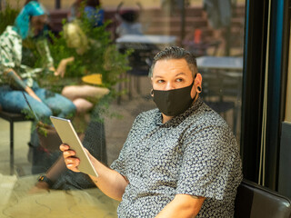 Shot of a man in a medical mask in a cafe  with a tablet - new normal