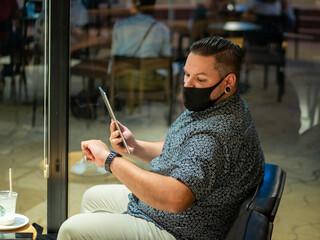 Shot of a man in a medical mask in a cafe  looking at his  watch - new normal