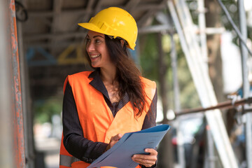 Portrait of a laughing caucasian female civil engineer wearing safety jacket and hardhat holding...