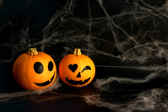 Little orange pumpkins with painted faces for Halloween with spiders on the net on black background