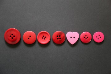 A closeup view of a row of red buttons, on a black background, including a pink heart.