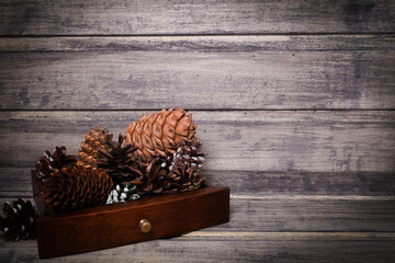 Christmas still life with cones in a wooden box on the wooden background. Copy space