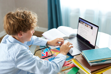 caucasian teen boy sit with laptop, studying online, enjoy education during quarantine. indoors
