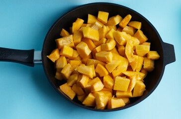 pieces of pumpkin in a black cast-iron pan, on a blue background. Seasonal vegetables, rich harvest, pumpkin sliced in a skillet. Diet, proper nutrition, healthy vegetables, vitamins all year round