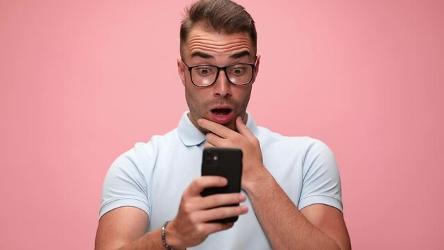 young handsome casual guy scratching his face while looking at his phone, being shocked and angry, slapping his face and waving his head