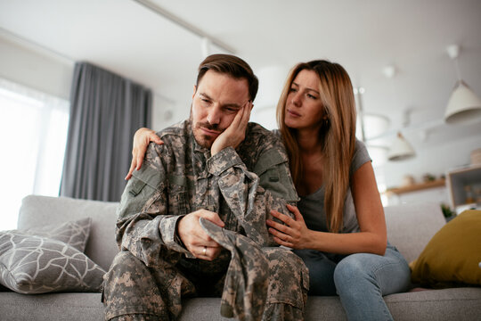 Depressed soldier sitting on sofa with his wife. Young marine having PTSD..