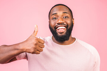 Portrait of cheerful, positive, handsome man with black skin, beaming smile in casual showing thumb up with finger to the camera isolated on pink background.