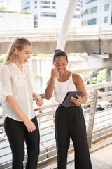 Businesswoman Showing Digital Tablet To Female Colleague On Walkway Bridge In City