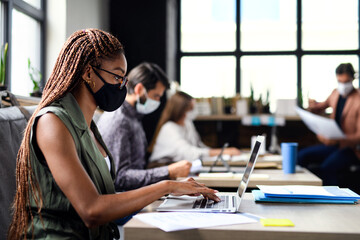 Business people with face masks indoors in office, back to work after coronavirus lockdown.