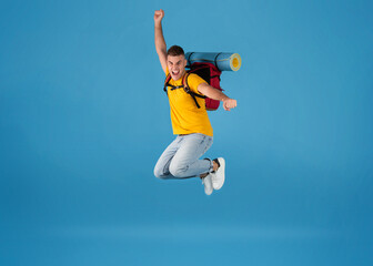 Excited young Caucasian tourist with camping equipment jumping on blue studio background